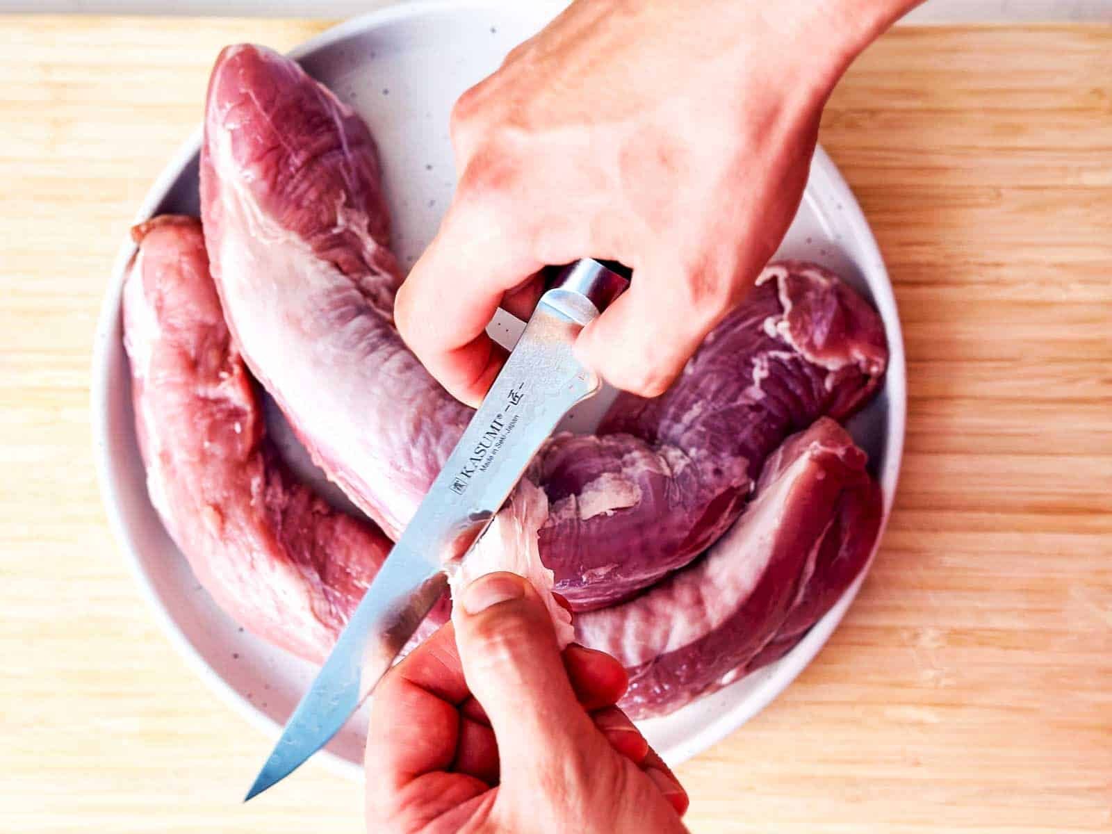 overhead view of male hands slicing silver skin off of pork tenderloin