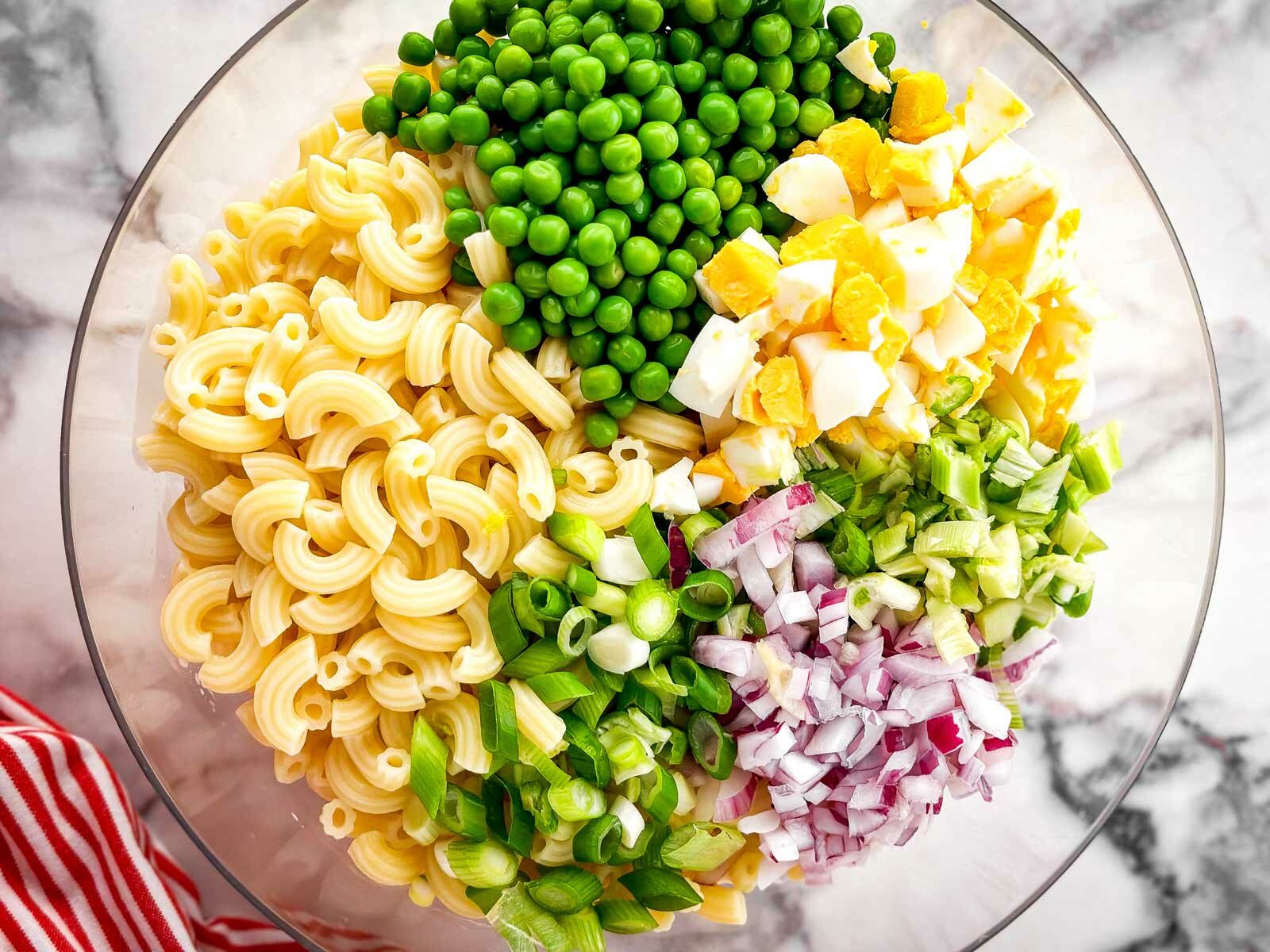 overhead view of ingredients for tuna macaroni salad in clear glass bowl