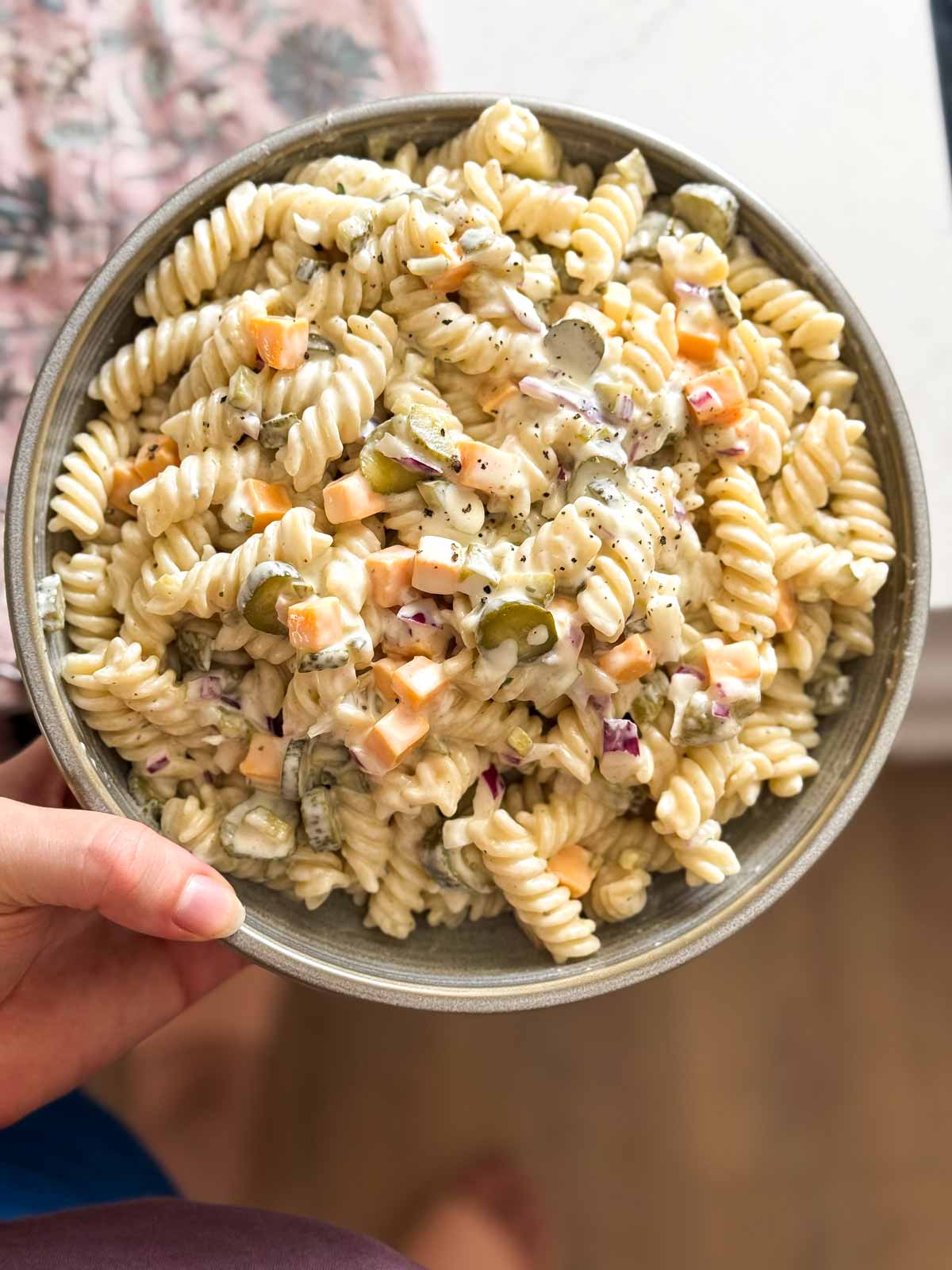 female hand holding a bowl of pasta salad