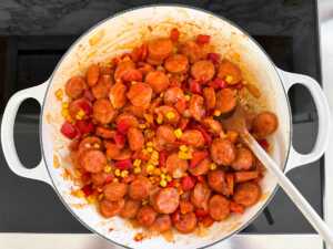 kielbasa and vegetables cooking in skillet with tomato paste and seasoning