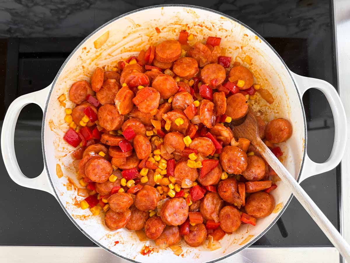kielbasa and vegetables cooking in skillet with tomato paste and seasoning