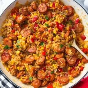 skillet kielbasa and rice being served with fresh herbs
