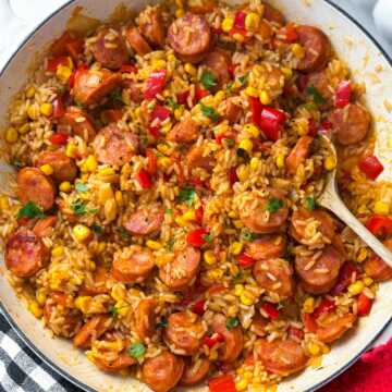 skillet kielbasa and rice being served with fresh herbs