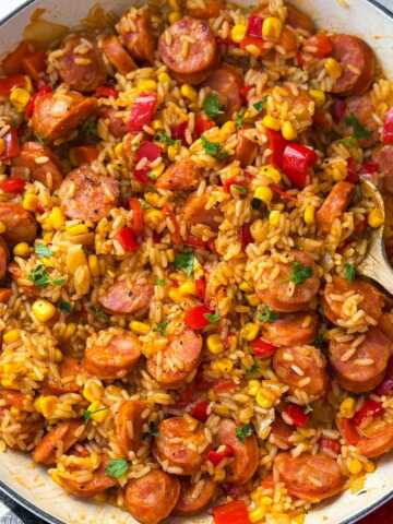 skillet kielbasa and rice being served with fresh herbs