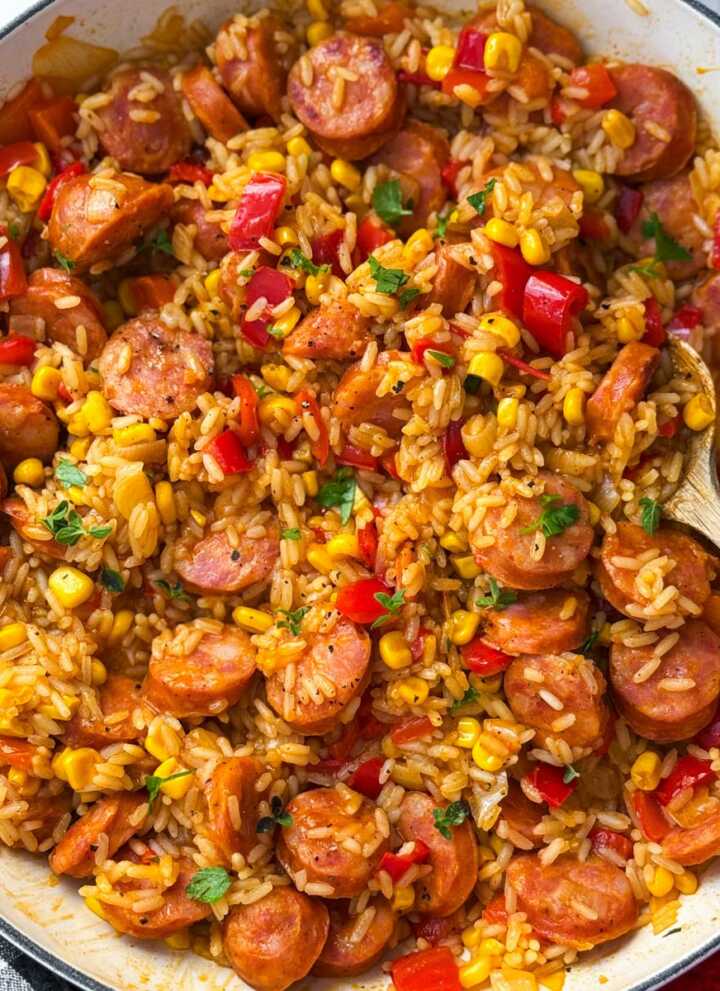 skillet kielbasa and rice being served with fresh herbs