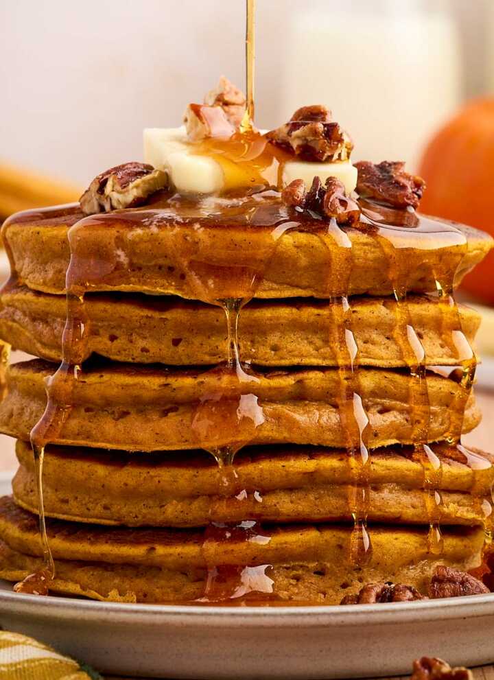 stack of pumpkin pancakes with syrup pouring over