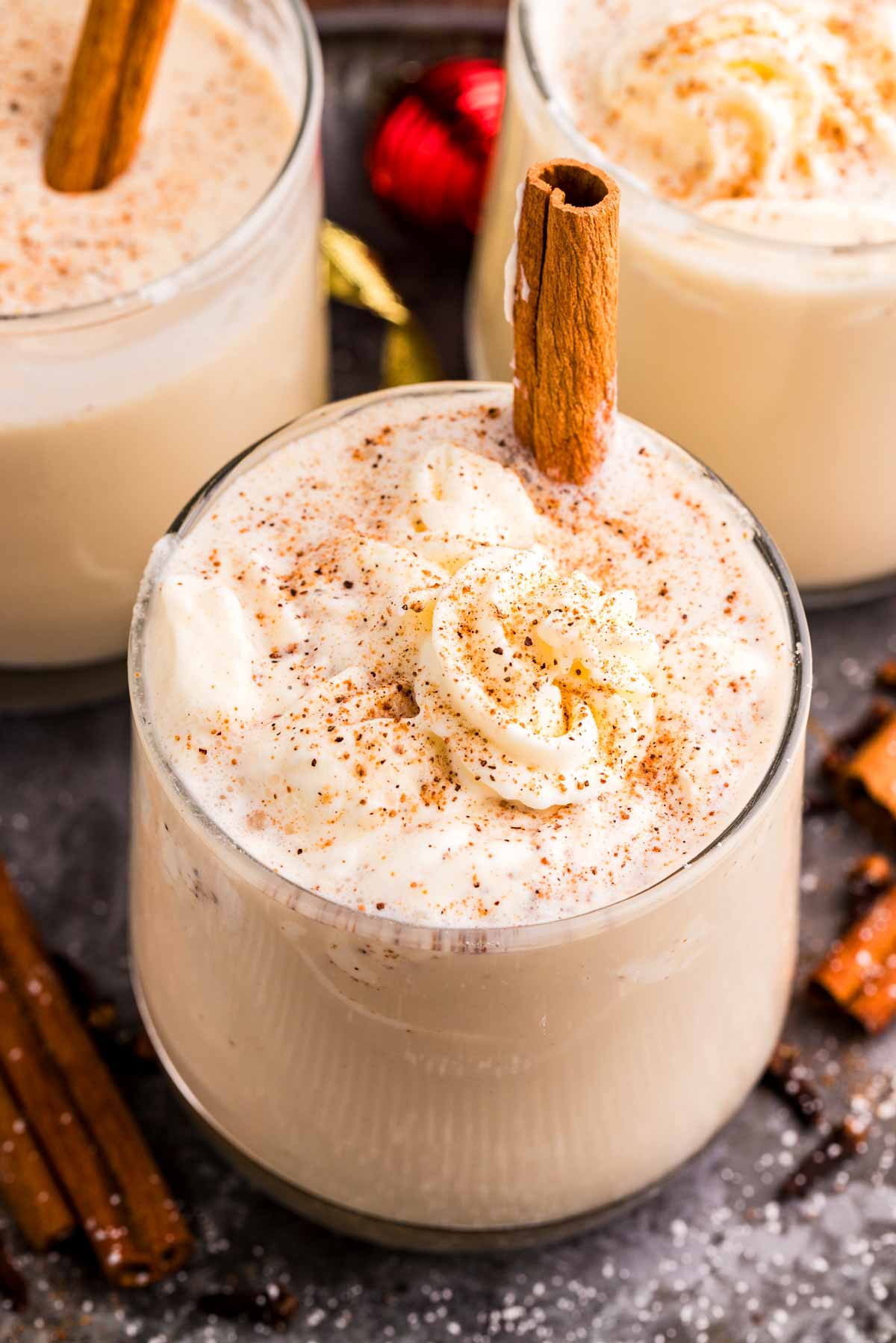 glasses of eggnog served with whipped cream and cinnamon sticks
