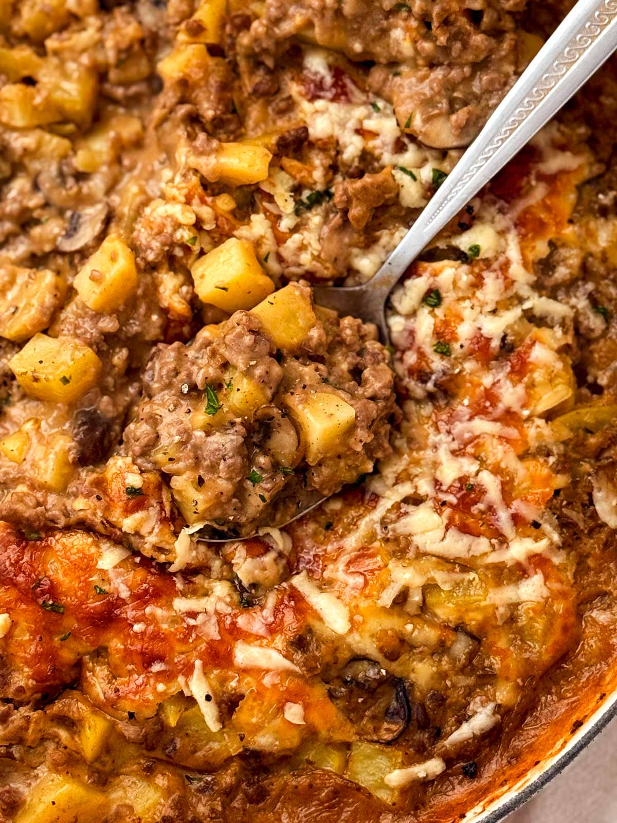 close up of a spoon scooping up ground beef and potato casserole