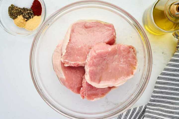 Pork chops tossed with oil in a glass bowl.