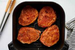 Pork chops in an air fryer basket.
