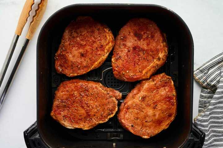 Pork chops in an air fryer basket.