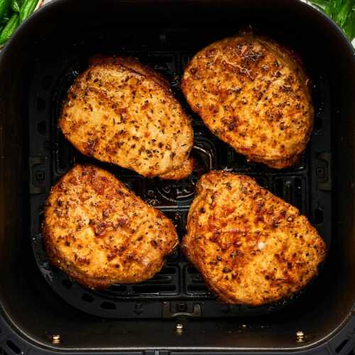 Pork chops in an air fryer basket.