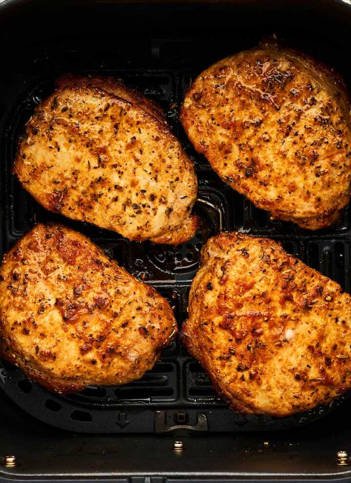 Pork chops in an air fryer basket.