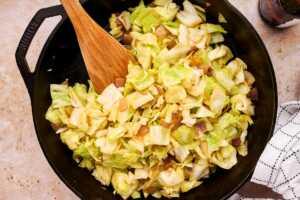 Sautéed cabbage in cast iron skillet with wooden spoon stuck in.