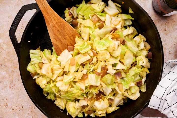 Sautéed cabbage in cast iron skillet with wooden spoon stuck in.