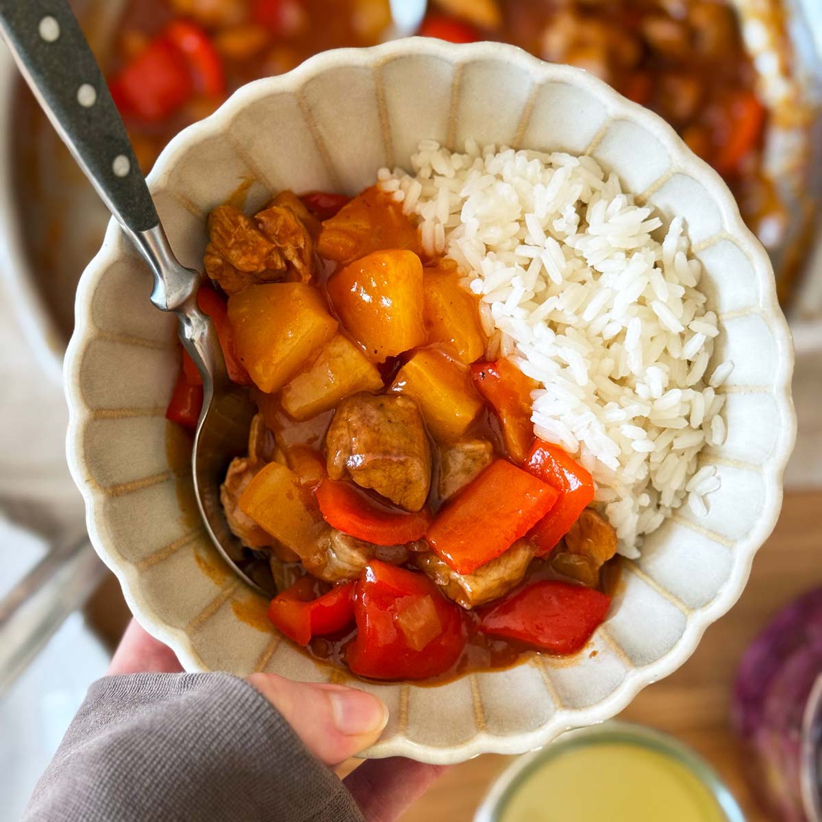 Holding a bowl with sweet and sour pork and rice.