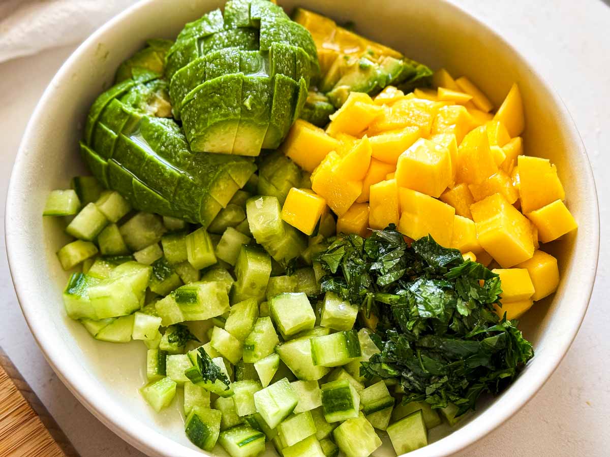 Chopped avocado, cucumber, mango and cilantro in a bowl.