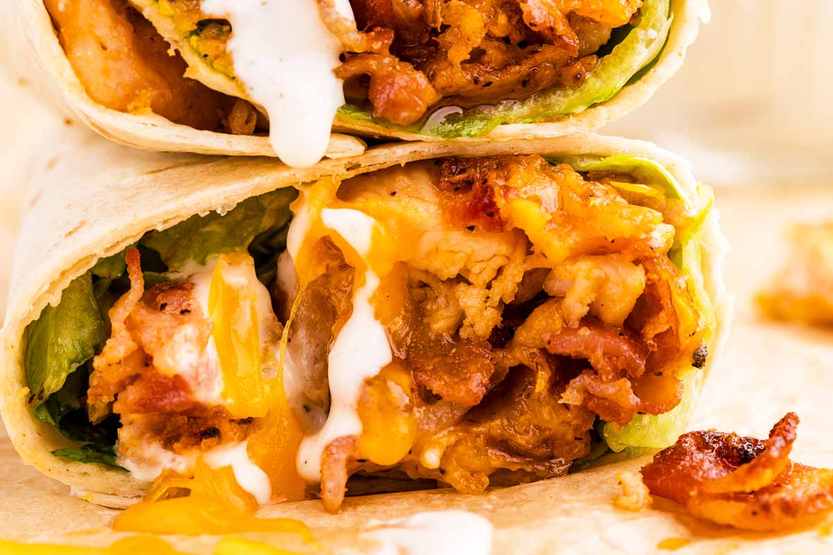 Close up view of a halved chicken wrap with lettuce, bacon, cheddar and ranch dressing.