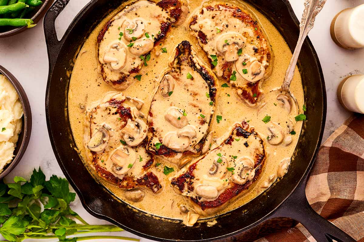 Serving creamy mushroom pork chops in a cast iron skillet.