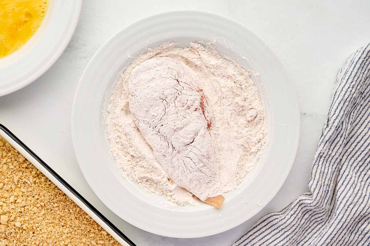 Chicken breast cutlet in a bowl with cornstarch.