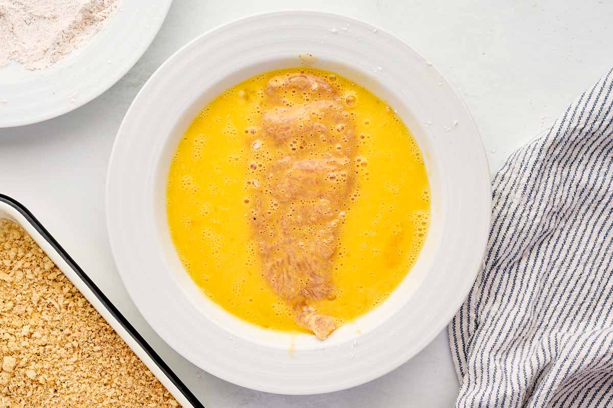 Chicken breast cutlet in a bowl with egg wash.