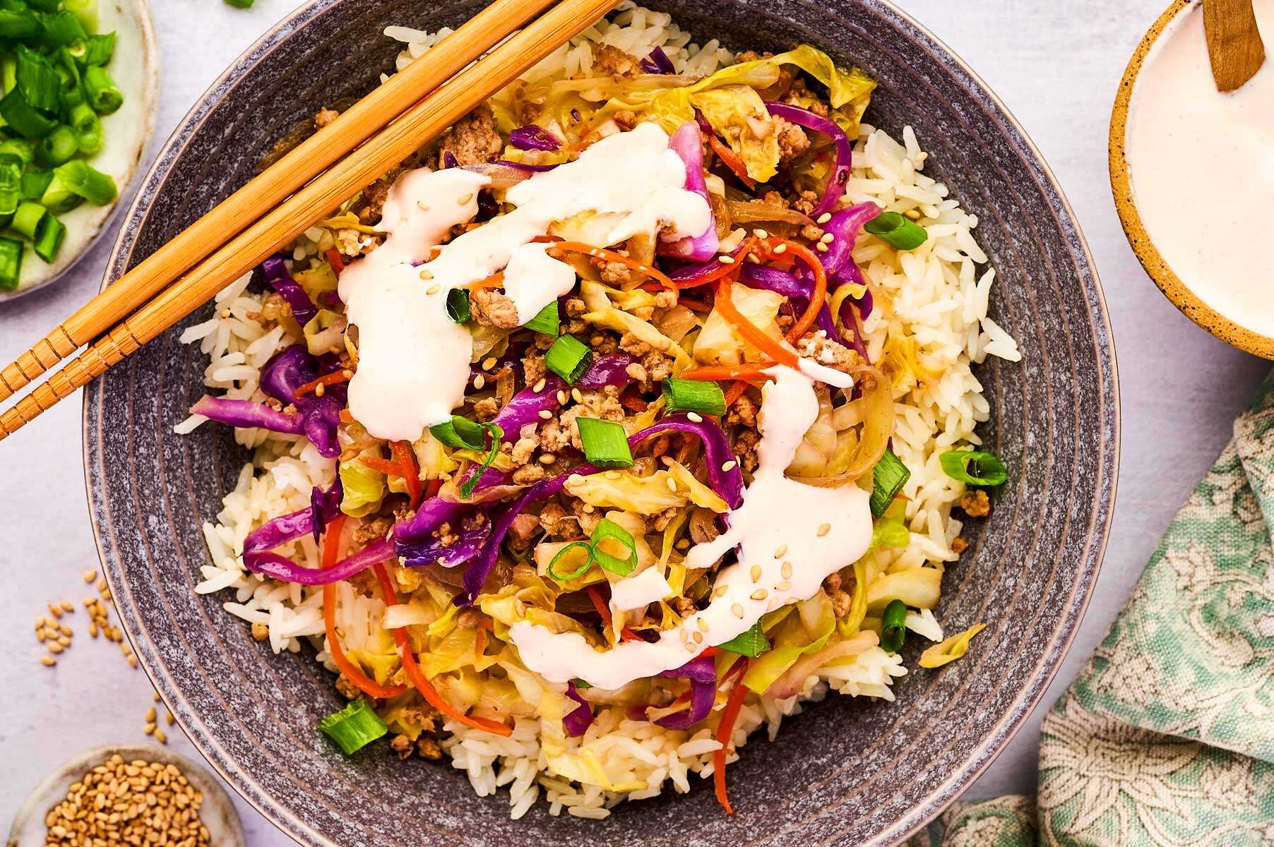 Serving egg roll in a bowl over rice with sriracha sour cream.
