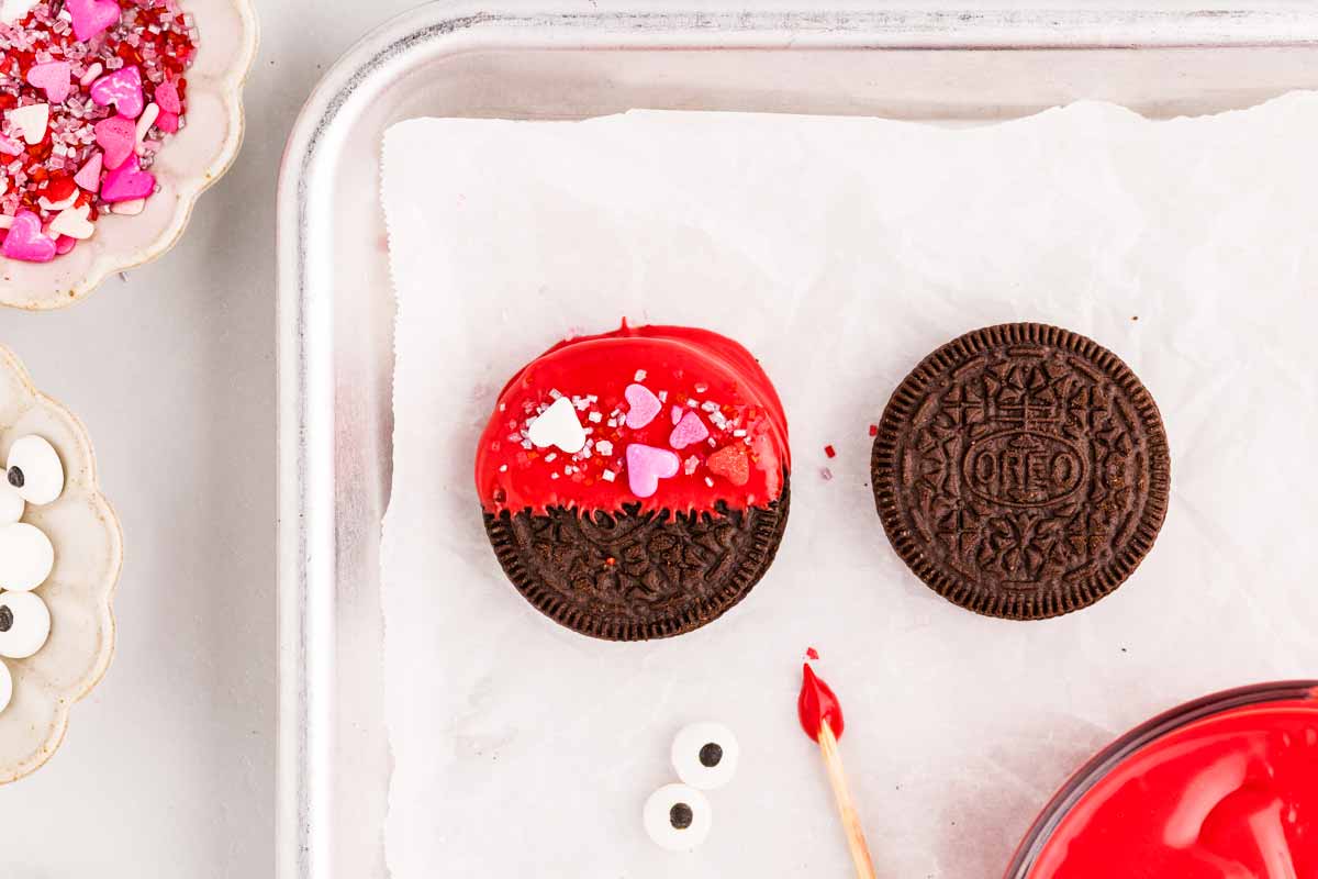 Decorating red candy melt covered Oreo with sprinkles.