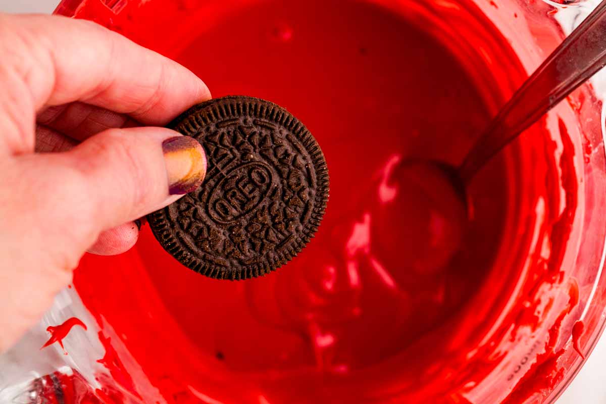 Holding an Oreo cookie over a bowl of red candy melts.