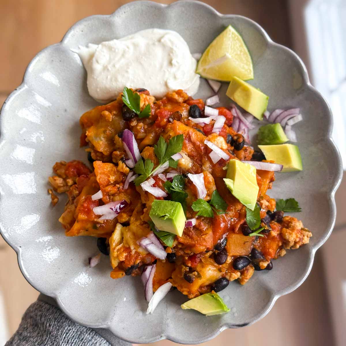Holding a plate of turkey enchilada skillet casserole.