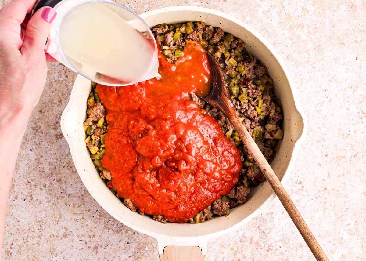 Pouring pasta water into a skillet with browned ground beef and tomato sauce.