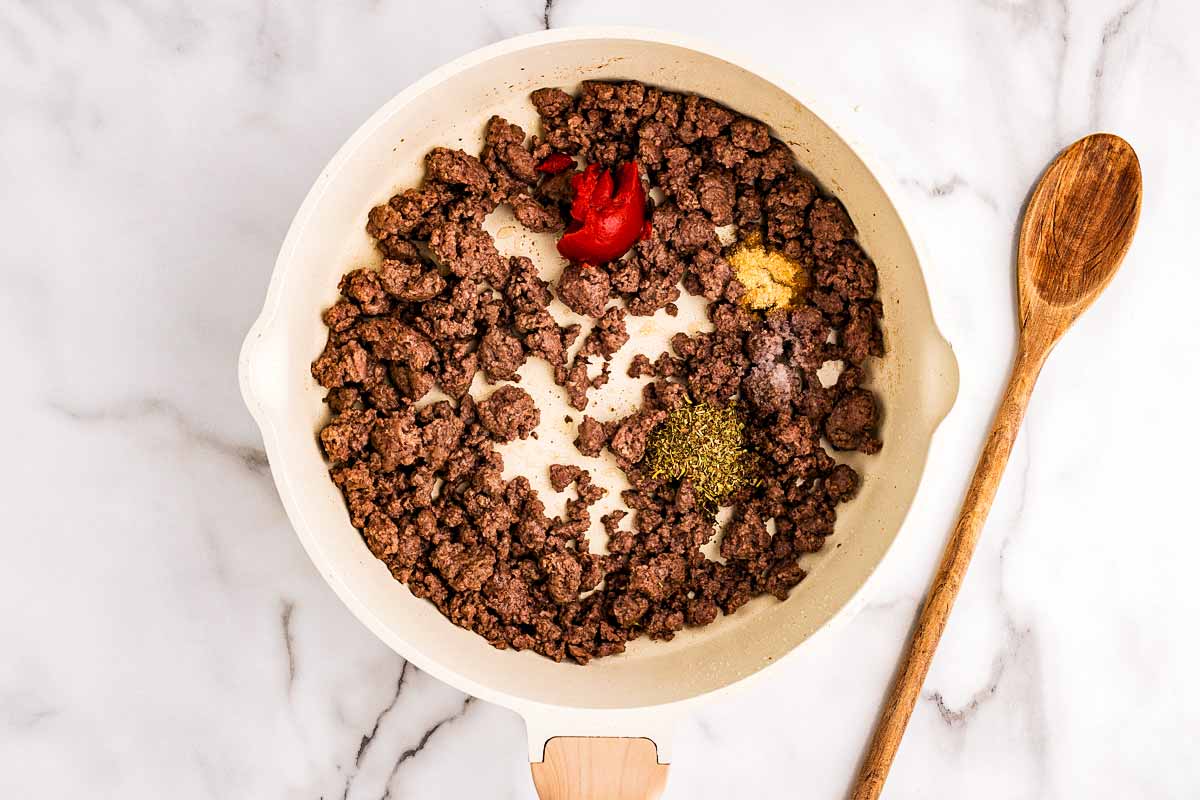 Browned beef in a skillet with tomato paste.