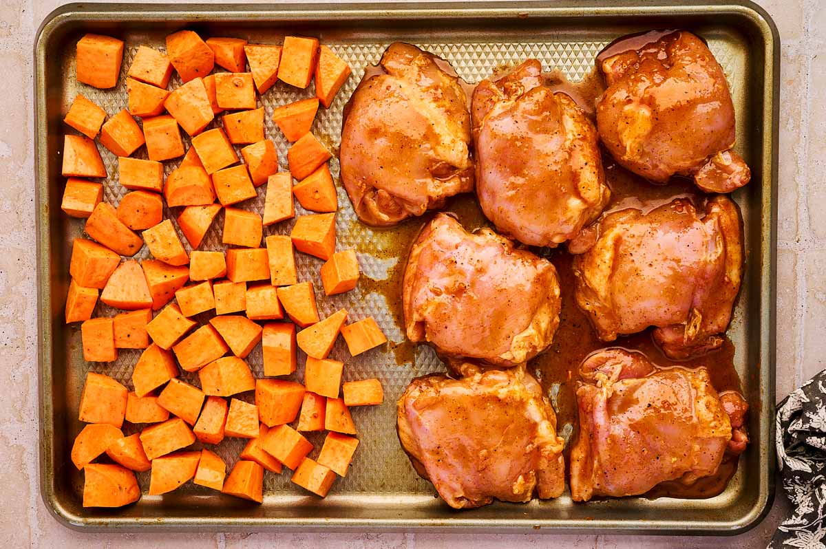 Sweet potato cubes and chicken thighs on a sheet pan.