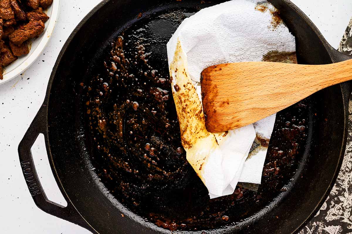 Wiping a cast iron skillet with paper towels.