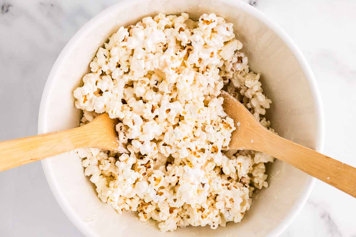Tossing popcorn and white chocolate with wooden spoons.