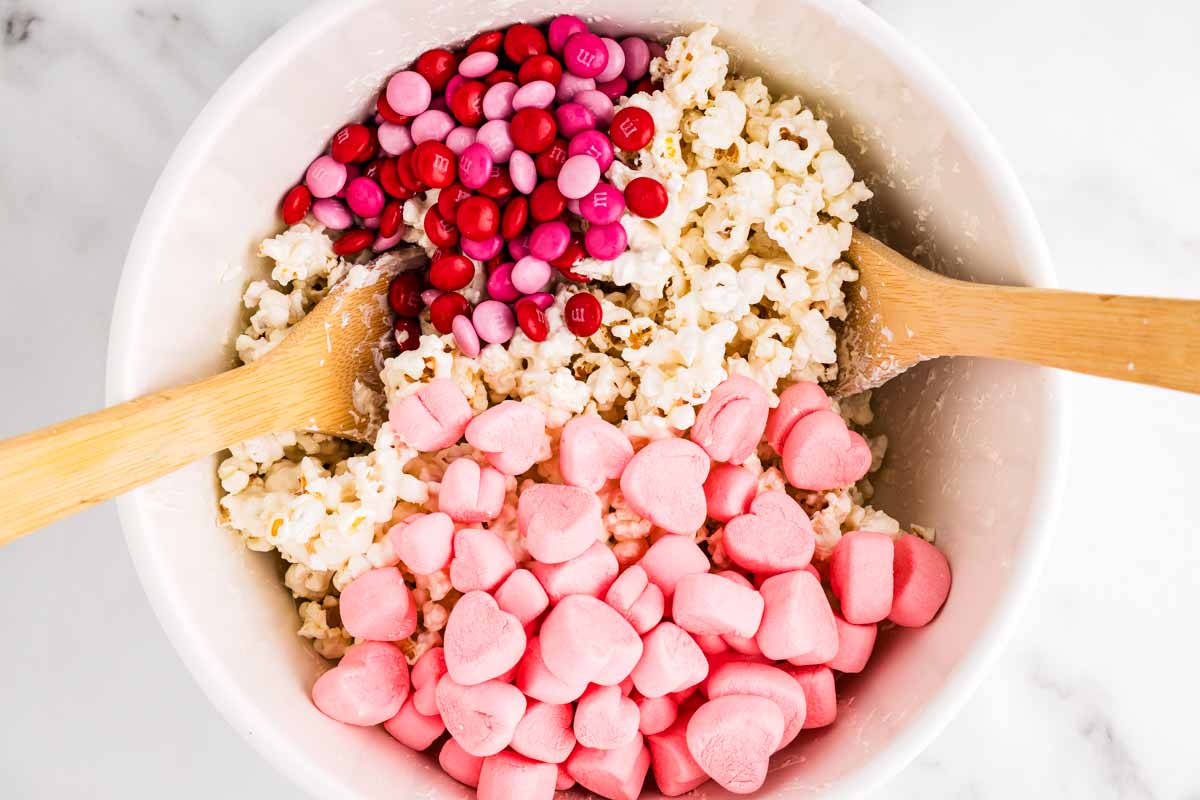 Adding heart marshmallows and Valentine's M&Ms to popcorn in a bowl.
