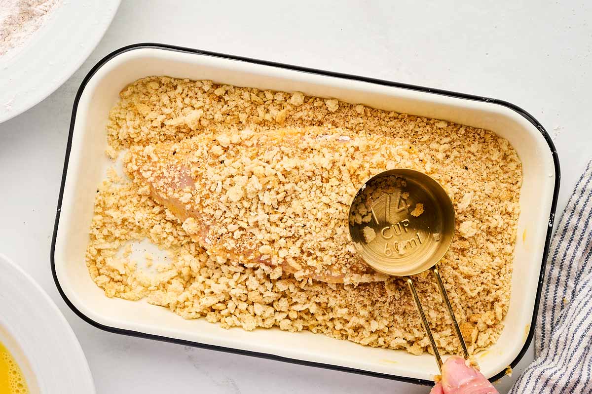 Pressing panko on a breaded chicken breast cutlet.