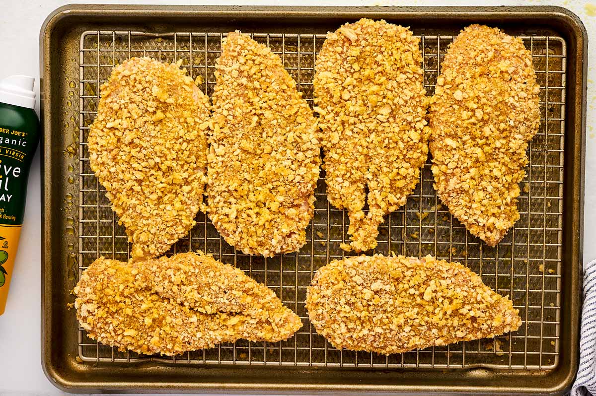 Breaded chicken cutlets on a rack set over a baking sheet.