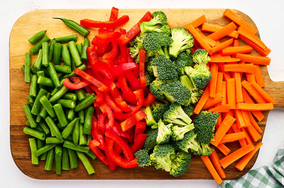 Cut up vegetables on a wooden cutting board.