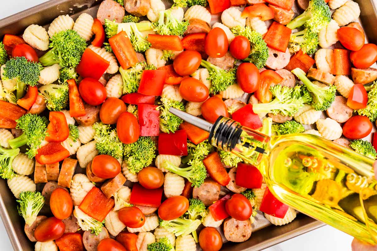 Pouring olive oil over sheet pan gnocchi.