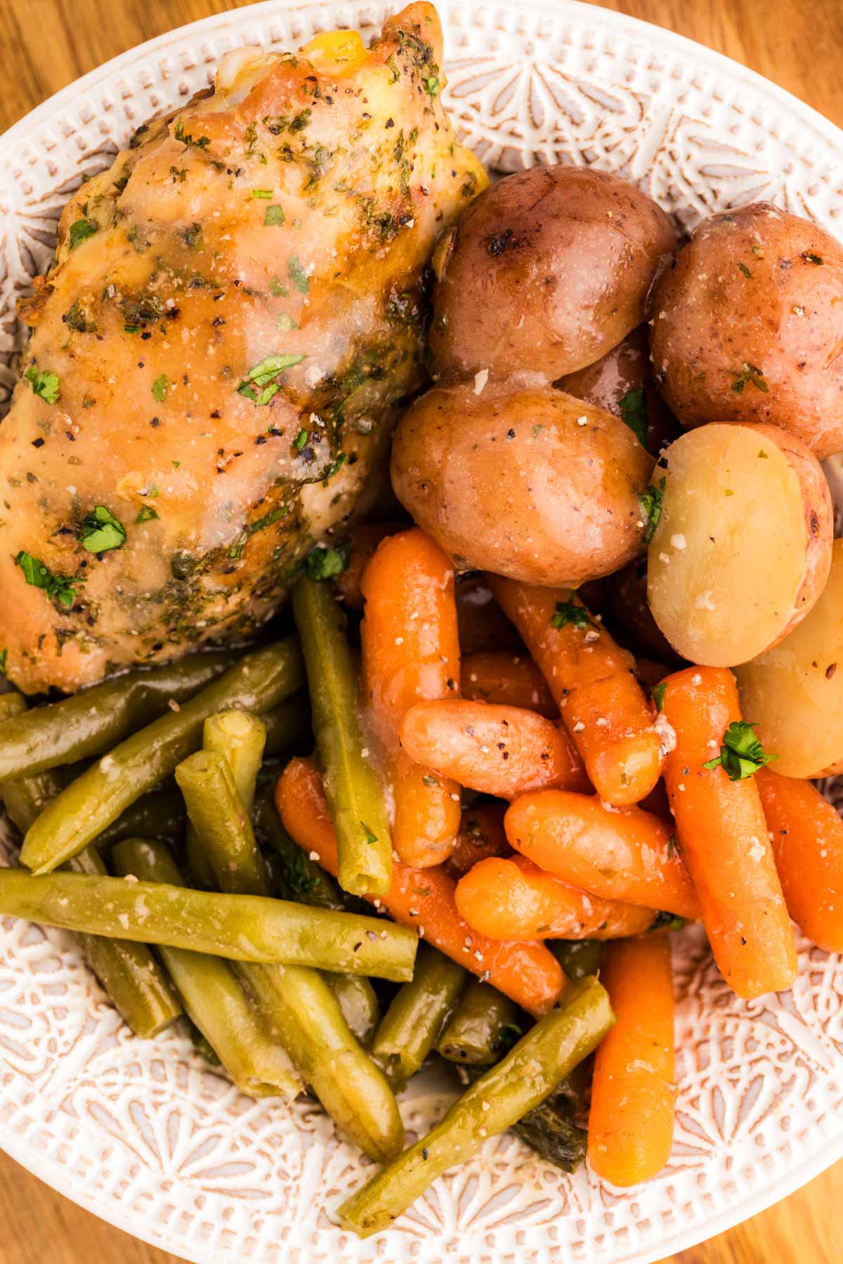 Plate with carrots, potatoes, green beans and chicken thigh.