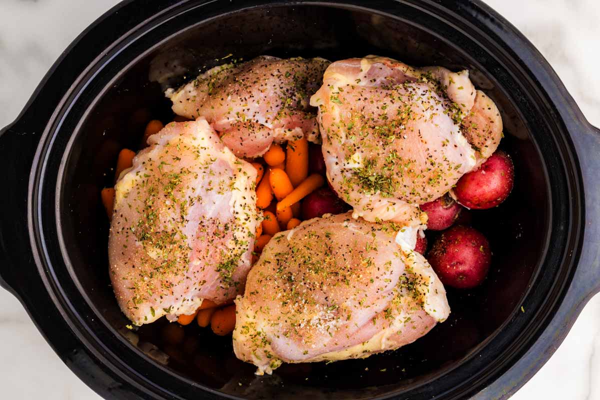 Uncooked chicken and vegetables in a slow cooker.