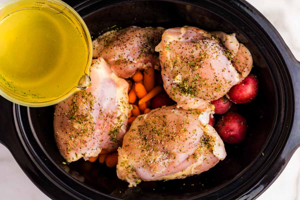 Pouring broth into a slow cooker with chicken and vegetables.