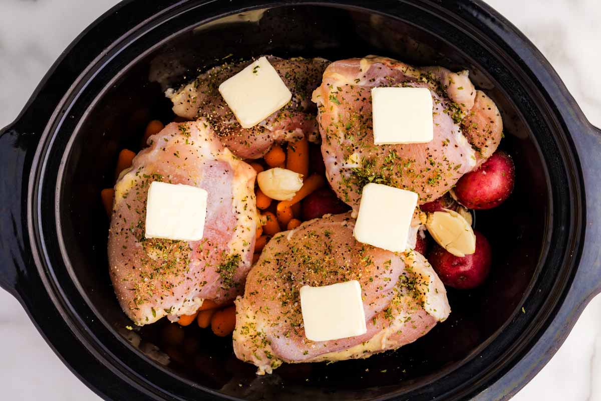 Butter pats on raw chicken and vegetables in slow cooker.