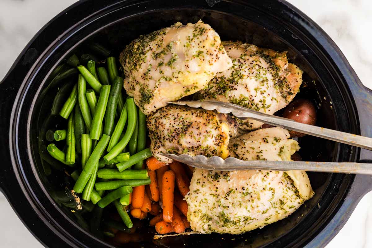 Arranging half-cooked chicken and vegetables in slow cooker.