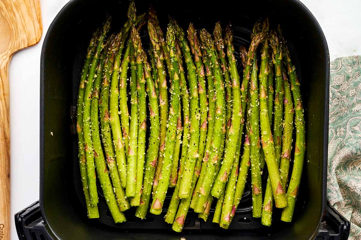 Air fryer basket with raw asparagus.