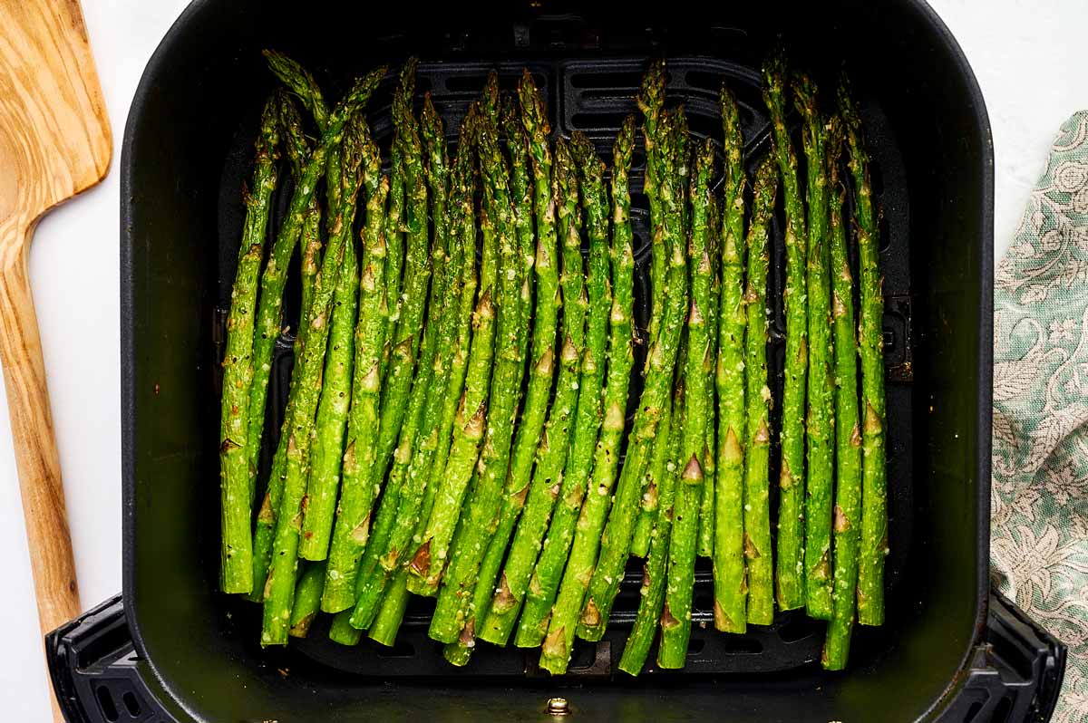 Air fried asparagus stalks in an air fryer basket.