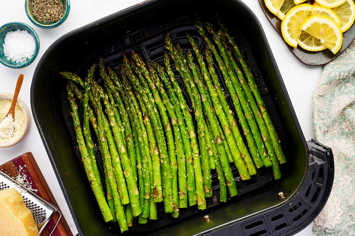 Air fryer basket filled with air fried asparagus stalks.