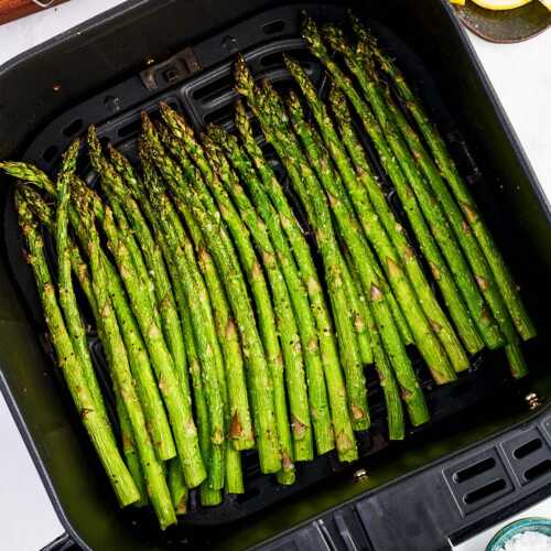 Air fryer basket filled with air fried asparagus stalks.