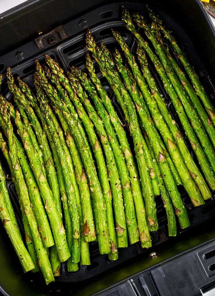 Air fryer basket filled with air fried asparagus stalks.