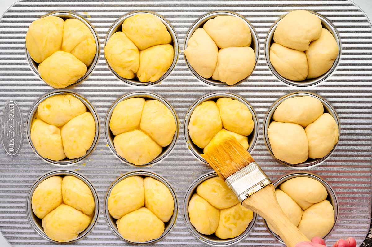 Egg washing cloverleaf dinner rolls before baking.